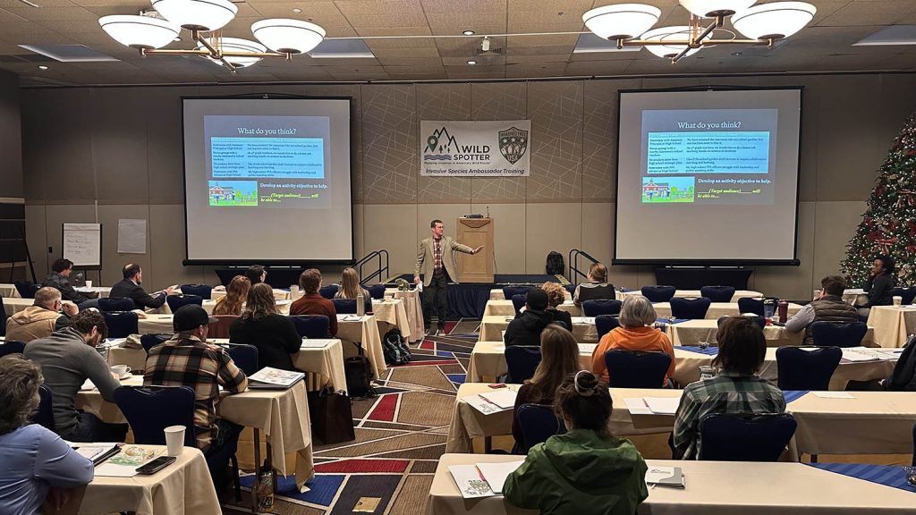 Gentleman in front of a podium speaking to a group of people attending a meeting.